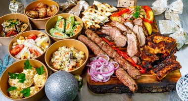 Ahşap tabakta sunulmuş rengarenk et, sebze ve salatalar. Dağınıklık, aile ve arkadaşlarla kutlama yapmak için mükemmel bir şenlik olduğunu gösteriyor..