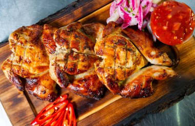 Yumuşak ızgara tavuk parçaları, taze sebzeler, baharatlı bir sos ve dilimlenmiş kırmızı soğan eşliğinde ahşap bir tabakta sergilenir. Bu lezzetli yemek tat ve aromayı davet ediyor..