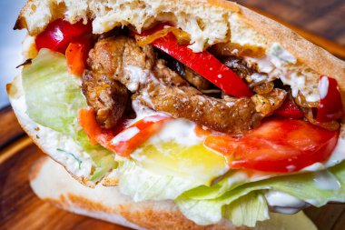 Yumuşak ızgara et, canlı kırmızı biber dilimleri, marul, domates ve üzerine kremalı sos serpiştirilmiş yumuşak ekmek ekmeği ile dolu doyurucu bir sandviç..