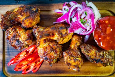 Sulu ızgara tavuk kanatları ahşap bir tabakta düzenlenir. Yanında bir dilim kırmızı soğan, taze biber ve küçük bir kase keskin sos var. Bu yemek lezzetli tatlar vaat ediyor..