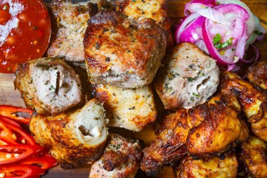 Taze tavuk ve domuz eti de dahil olmak üzere çeşitli ızgara etler sergilenirken, kırmızı soğan, sos ve dilimlenmiş kırmızı biberle servis ediliyor. Parlak renkler iştah açıcı bir sunum oluşturur.