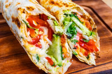 Kızarmış tortilla 'ya sarılı kıvırcık salata, domates ve peynirin olduğu bir dürümün yakın plan çekimi. Renkler parlak ve iştah açıcı. Taze malzemelerin altını çiziyorum..