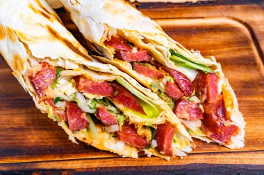 İki ızgara dürüm lezzetli et ve taze sebze karışımı ile doldurulur. Yemek ahşap servis panosunda, canlı malzemeler sergileniyor ve iştah açıcı bir sunum yapılıyor..