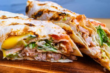 Tahta bir tahtanın üzerinde servis edilen tavuk, sebze ve sosla dolu taze yapılmış iki tortilla yakın plan görüntüsü. Canlı renkler ve dokular çekici bir yemek seçeneği sunuyor.