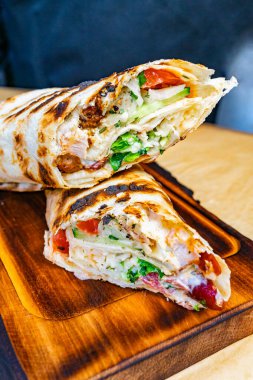 Bu tabakta bol bol doldurulmuş et, taze marul, domates ve otlar yer alıyor. Hepsi de ahşap bir tahtanın üzerinde gevrek bir ekmek içinde..