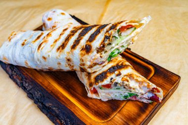 Tahta bir tahtanın üzerinde taze sebze ve etle dolu lezzetli bir ızgara dürüm sunulur. Altın sarısı şalter iştah açıcı görünüyor, öğle yemeğinde sıradan bir yemek için mükemmel..