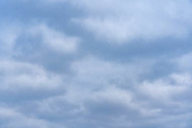 Mavi ve gri tonlarında kalın bulutlarla dolu bulutlu bir gökyüzü. Atmosfer sakin ve sakin görünüyor, aşağıdaki manzaraya sakin bir hava katıyor..