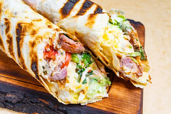 Tahta bir tahtanın üzerinde et, sebze ve peynirle dolu iki ızgara burrito. Yemek canlı renkler ve dokular sergiliyor, tazelik ve lezzeti vurguluyor.