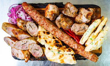 Izgara etler ahşap bir tabakta çeşitli sosisler, taze et parçaları ve soğan ve biberle süslenerek lezzet katılıyor..