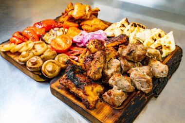 Canlı bir tabakta tavuk ve domuz eti de dahil olmak üzere çeşitli ızgara etlerin yanı sıra kırmızı soğan, dolmalık biber ve domates gibi renkli sebzeler yer alıyor..