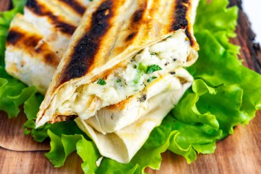 Taze ızgara pakette yumuşak tortilla tabakalarının arasına yerleştirilmiş taze tavuk ve otlar yer alıyor. Canlı, yeşil bir kıvırcık kıvırcık kıvırcık kıvırcık yatakta uzanır ve tazeliğini ön plana çıkarır..