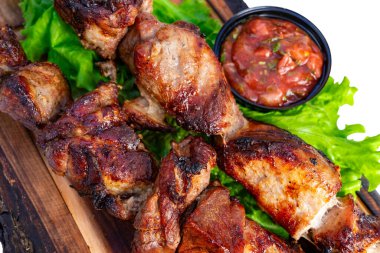 Lezzetli ızgara kebap şişleri, canlı yeşil marullarla dolu ahşap bir tabakta servis edilir. Küçük bir kase taze salsa yemeğin tadını artırmak için eşlik eder..