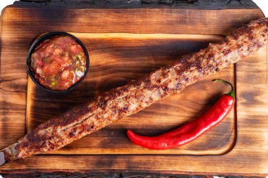 Lezzetli bir kebap, yanında baharatlı biber ve bir kase taze salsa ile ahşap bir tahtanın üzerinde dinlenir. Yaz barbeküsünde ya da dışarıda eğlenmek için mükemmel..