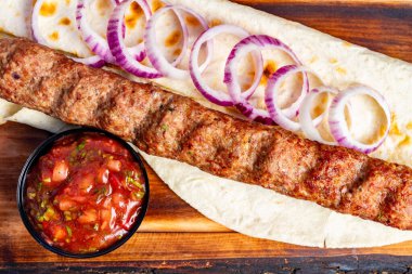 Izgara bir kebap, üzerinde mor soğan dilimleri olan sıcak bir ekmek üzerinde dinlenir. Küçük bir kase enerjik salsa, renkler ve tatlar ekleyerek yemeğe eşlik eder..