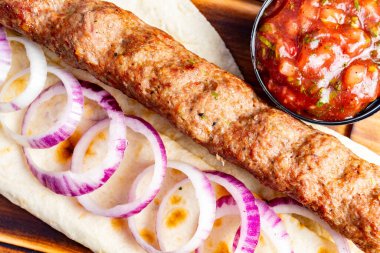 Lezzetli bir kebap ince dilimlenmiş soğanla süslenmiş yumuşak bir ekmeğin üzerinde durur. Küçük bir kase taze salsa, canlı renk ve tat ekleyerek yemeği tamamlar..