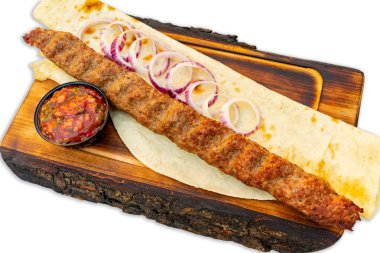 Uzun, sulu bir kebap, ince dilimlenmiş soğanlar ve küçük bir kase baharatlı sos eşliğinde servis tabağında dinlenir. Sıcak ekmek yemeği tamamlar, lezzeti arttırır..