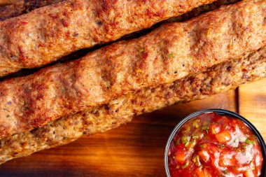 Lezzetli kebaplar, mükemmel ızgara, küçük bir kase canlı salsa ile birlikte ahşap bir tabakta dinleniyor. Yaz barbeküsü ya da lezzetli bir akşam yemeği için mükemmel..