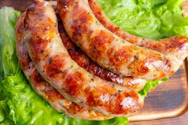 Lezzetli ızgara sosisler canlı yeşil marul yatağında dizilmiş. Sulu bağlantılarda altın-kahverengi bir renk ve umut verici lezzetli lezzetler ve aromalar var..