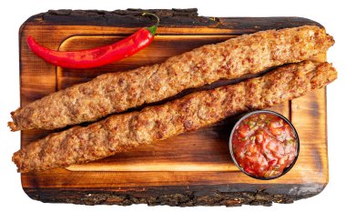 Sulu ızgara et şişleri, küçük bir kase taze salsa ve canlı kırmızı acı biberle birlikte ahşap bir tahtanın üzerinde kaplanarak ağız sulandıran bir mutfak lezzeti sunar..