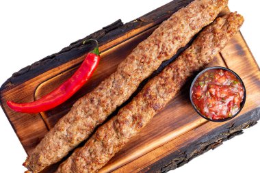 İki mükemmel ızgara kebap bir kase taze salsa ve canlı kırmızı biberin yanında ahşap bir tabakta yatıyordu. Bu ağız sulandırıcı yemek zengin tatlar ve dokular sergiliyor..