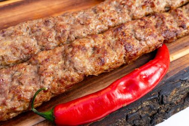 Sulu ızgara kebaplar, canlı kırmızı bir biberin yanında, ahşap bir tahtanın üzerinde dinleniyor. Ağız sulandırıcı bir yemek sergiliyorlar. Yaz barbeküsünde tadını çıkarmaya hazır..