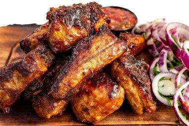 Lezzetli yanmış domuz kaburgaları ahşap bir tahtanın üzerinde üst üste yığılmış taze soğan dilimleri ve canlı bir sos, ağız sulandıran bir barbekü ziyafetini çağrıştırıyor.