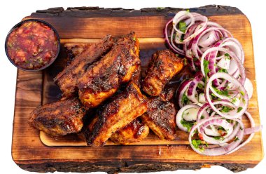 Sulu ızgara pirzola, taze soğan ve salatalık dilimleriyle birlikte ahşap bir tahtanın üzerinde baharatlı sosla servis edilir..