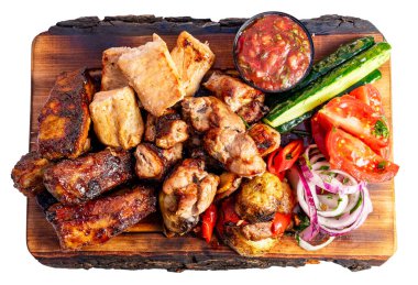 Taze sebzeler ve bir kase salsa eşliğinde ahşap bir tabakta samimi bir ızgara et seçimi düzenlenir. Canlı renkler, lokantalar için davetkar bir sunum oluşturuyor..