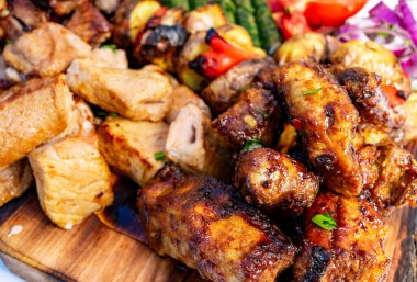 Ahşap bir tabakta tavuk, biftek ve sebzeler de dahil olmak üzere rengarenk bir ızgara et çeşidi sunuluyor. Bu canlı yemek arkadaşlarla yaz barbekülerinin neşesini gösteriyor..