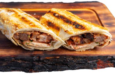 İki ızgarada ahşap bir tahtanın üzerinde, içi taze et ve taze malzemelerle dolu, altın-kahverengi, mükemmel kavrulmuş bir dış görünüş sergiliyor..