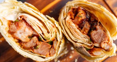 Ahşap bir tahtanın üzerinde iki doyurucu et ambalajı ustaca sunuluyor. Lezzetli malzemeler ve canlı renkler sergileniyor. Tatmin edici bir yemek için mükemmel..