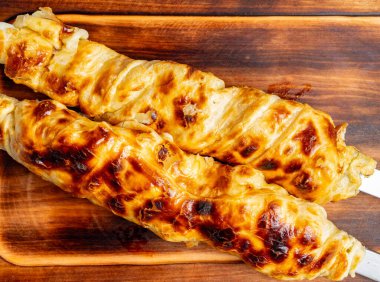 İki ızgara şiş altın sarısı, kıtır kıtır bir dış görünüş sergiliyor, zengin bir dolguyu ortaya çıkarıyor. Geleneksel yemek bir tahta kesme tahtasının üzerinde oturur ve yaz ziyafetinde iştah açıcı cazibesini vurgular..