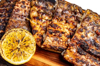 Lezzetli ızgara balık filetoları ahşap bir tahtaya güzelce dizilir ve çıtır çıtır dokuları sergilenir. Yanlarında, kömürleşmiş bir limon turunçgil patlaması sunar. Yaz yemeği için mükemmel..