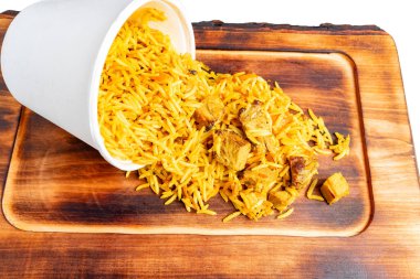 Altın pirinç ve et parçaları beyaz bir konteynırdan ahşap bir yüzeye dökülerek canlı ve iştah açıcı bir karmaşa yaratır. Renkler ve dokular izleyicinin iştahını çekiyor..