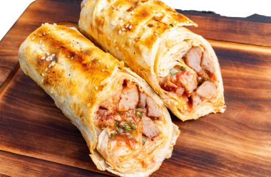 İki taze ızgara, ahşap bir tahtanın üzerinde oturmuş et, sebze ve sosun içini gösteriyor. Altın kabuk mükemmel bir şekilde kızartılmış, iştah açıcı bir görünüm yaratıyor..