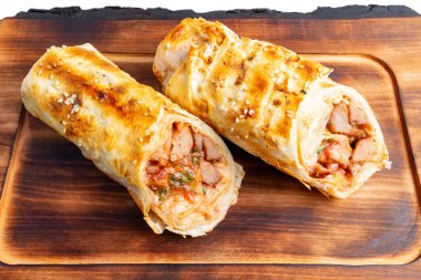 Tahta bir tahtanın üzerinde içi taze tavuk ve renkli sebzelerle dolu iki altın sarısı. Susam tohumları bu lezzetli yemeğe lezzetli bir çıtır ekliyor..