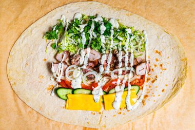 Taze sebzeler, taze ızgara tavuk ve kremalı sos ustalıkla bir tortilla üzerinde düzenlenir. Bu canlı ambalajda renkli malzemeler sergileniyor..