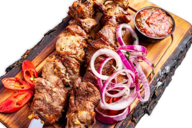 Sulu ızgara et şişleri ahşap bir tahtada servis edilir, dilimlenmiş soğanlar, taze biberler ve yanında canlı bir sos ile süslenir, yemek sırasında lezzetli bir mutfak deneyimini davet eder..