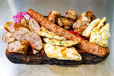 Izgara etler, sosis ve terbiye edilmiş tavuk dahil, ahşap bir tabakta güzelce düzenlenmiştir. Taze ekmek ve süslemelerle birlikte, tabak canlı renkler ve dokular sergiliyor..