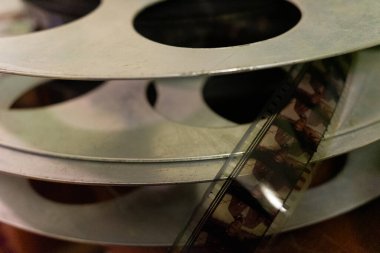 Metal film makaralarının bir araya toplanması ve bir makaranın klasik filmin bir bölümünü göstermesi. Sahne, yumuşak ışıklandırmadaki sinematik ekipmanların dokusunu ve tarihini yakalıyor..