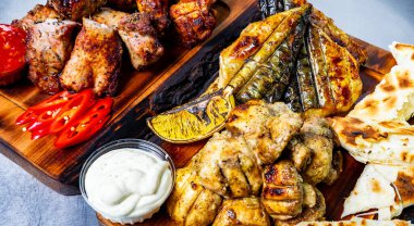 Güzelce düzenlenmiş bir tabakta tavuk ve balık da dahil olmak üzere taze kesilmiş sebze ve kremalı sosla birlikte bir dizi ızgara et yer alıyor. Canlı renkler sunumu güçlendirir.