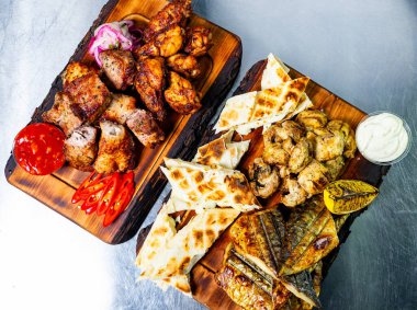 Ahşap tabakta, ızgara tavuk, balık ve lezzetli kenarlardan oluşan lezzetli bir karışım. Taze sebze ve soslar sunuma canlılık katıyor..