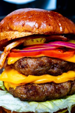 İki köfteli, erimiş peynirli, gevrek pastırmalı ve taze sebzeli duble çizburger, marul yaprağının üzerinde dinleniyor. Yaz barbeküsü için mükemmel..