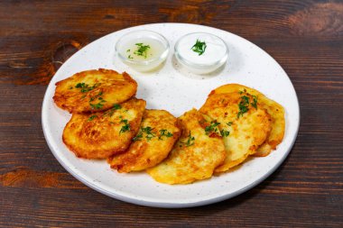 Altın rengi patatesli krepler taze otlarla süslenmiş beyaz bir tabakta, yanında da iki kase kremalı sos. Bu lezzetli yemek paylaşmak ya da tek başına eğlenmek için mükemmel..