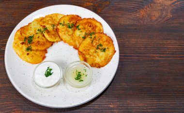 Taze yapılmış patatesli gözlemeler iki küçük kase kremalı sos eşliğinde kırsal bir tabakta güzelce düzenlenir. Yemek otlarla süslenir, davetkar bir sunum oluşturur..