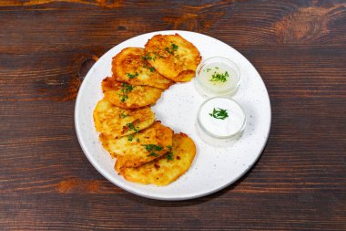 Altın-kahverengi patatesli krepler beyaz bir tabakta taze otlarla süslenir. İki küçük kase krema tabağa eşlik ederek, onu lezzetli bir yemek seçeneği yapıyor..