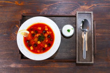 Güçlü bir kırmızı borç, limon ve otlarla süslenmiş sebze ve zeytin içerir. Yanında küçük bir kase krema, ahşap bir tepside çatal bıçaklarla zarif bir şekilde düzenlenir..