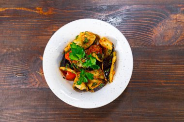 Taze otlarla süslenmiş kabak, patlıcan ve kiraz domatesleri de dahil olmak üzere rengarenk sebze karışımı ahşap bir masada kırsal bir kasede sunuluyor..