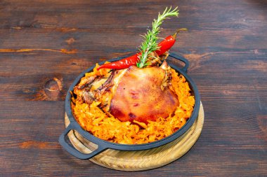 Güzel bir şekilde sunulmuş kızarmış domuz eti, baharatlı lahana yatağının üzerinde oturur. Kırmızı biber şeritleri ve biberiye filizi kırsal ahşap masa düzenine canlı renkler ekler..