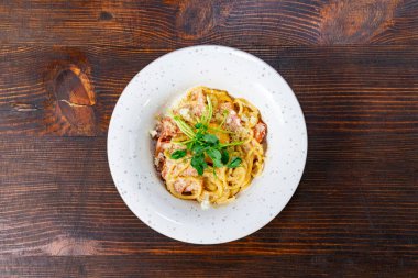 Otlarla süslenmiş bir tabak kremalı deniz ürünleri makarnası kırsal bir ahşap masada duruyor. Yemekler lezzet ve dokuların karışımını sergiliyor. Sıcak bir yemek deneyimi için mükemmel..